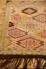Secured side and dark brown fringe on the vintage Jijim rug, with geometric red and gold patterns.