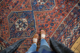 Vintage Persian Shiraz rug, overhead view of rust field pinwheel motifs and blue medallion.