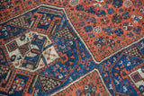 Close-up of vintage Shiraz rug with geometric medallion outline and pinwheel floral motifs in rust, blue.