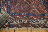 Vintage hand-knotted Shiraz rug corner: blue, rust, ivory geometric border and soft fringe.