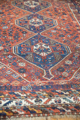 Vintage Shiraz carpet's geometric border, chestnut rust field, and sky blue pinwheel motifs.