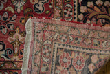 Vintage Mahal carpet corner folded, revealing brick red, charcoal floral patterns and woven base.