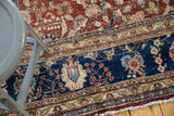 Vintage Kerman carpet's navy border, blush, ivory floral bouquets, visible pile wear, tattered fringe.