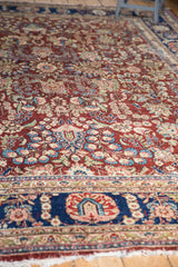 Vintage Kerman rug showing navy border, cherry red floral field, and tattered fringe.