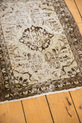 Beige and charcoal distressed Hamadan rug corner, showing worn pile and white fringe.