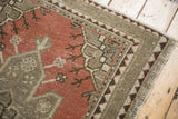 Distressed hand-knotted Oushak rug corner showing geometric border and worn brick red pile.