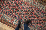 Person's foot on antique Kurdish runner, highlighting its cinnabar red field and floral botehs.