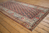 Detailed view of antique Kurdish rug corner showing geometric border and repeating boteh patterns.
