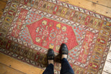 Vintage Melas rug corner: brick red field with blossomed motifs, pale bronze, and blue borders.