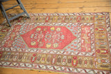 Vintage Melas rug corner, featuring secured edges, brick red field, bronze border, and even wear.