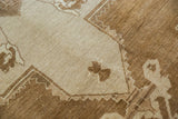 Detail of distressed Oushak carpet showing pale beige field, chocolate brown zigzag motif, and worn pile.