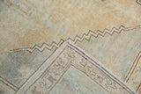 Distressed Oushak rug corner showing worn pale gold pile, geometric border, and zigzag stitched reverse.