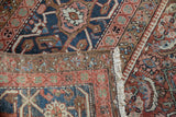 Secured edge, fringe, and Herati motif of a vintage Heriz carpet in navy and brick red.