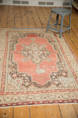Lower left corner of the distressed vintage Oushak rug, showing short fringe, pale cinnabar, and antique ivory border.