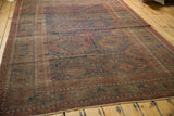Corner of antique Belouch carpet, geometric red and navy patterns on chestnut brown field.