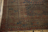 Antique Belouch carpet corner, displaying geometric chestnut, navy, and red motifs with even wear.