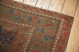 Visible knot head wear across the red, navy, and ivory geometric border of an antique Belouch carpet.