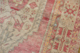 Distressed Oushak rug close-up: faded blush red, beige, oxidized silver geometric patterns, low pile.