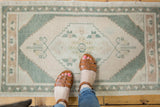 Feet in sandals on a vintage distressed Oushak rug with pale beige and celadon medallion.