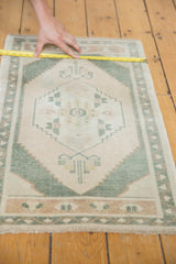Measuring the distressed pile of the vintage Oushak rug, showing ivory and pale green patterns.
