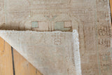 Curled distressed Oushak rug corner showing low pile, pale green accents, and ivory fringe.