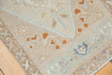 Distressed Oushak rug corner reveals ivory, terracotta, blue budded floral arabesque motifs and fringe.