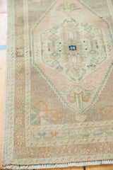 Distressed Oushak rug's intricate serrated stepped field with ivory, pale peach, and seafoam hues.