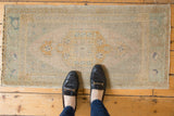 Distressed vintage Oushak mat runner with a central medallion and muted gold, silver, and sand tones.
