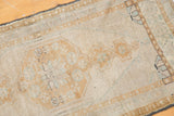 Angled detail of the distressed vintage Oushak rug showing pale bronze and seafoam geometric patterns.