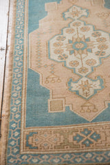 Scalloped aqua blue and sand floral pattern detail on a distressed vintage Oushak rug with selvage.