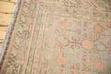 Distressed Khotan carpet corner showing pale red pomegranate design, silver tones, and visible wear.
