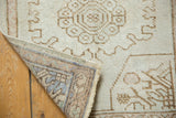 Distressed Oushak rug with detailed hand-knotted reverse, fringe, and faded ivory curvilinear motifs.