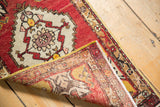 Curled corner of vintage Oushak rug showing ivory medallion, red field, hand-knotted reverse, and selvage.