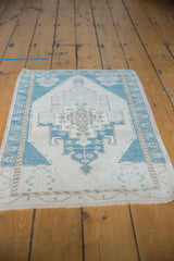 Distressed vintage Oushak rug corner showing low pile, geometric teal, ivory, and beige patterns.