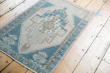 Distressed Oushak rug corner, geometric teal border, beige field, and germinating plant motif.