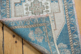 Distressed Oushak rug corner showing low pile, blue reverse, and pink selvage.