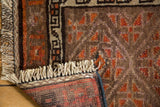 Hand-knotted Belouch rug: low pile, geometric pattern in orange and charcoal, ivory fringe, woven back.