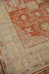 Distressed Khotan rug corner with a cherry red floral field and wide geometric beige border.