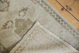 Distressed Oushak rug corner revealing low pile, hand-knotted reverse, and zig-zag border.