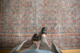 Person's feet on vintage distressed Mahal carpet, highlighting faded Herati pattern and soft texture.