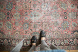 Distressed vintage Tabriz carpet with Safavid-inspired floral palmettes in pale raspberry and exposed foundation.