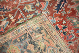 Vintage Heriz carpet corner reveals hand-knotted foundation, green edge, and red-blue geometric pattern.