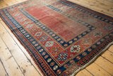 Antique Caucasian rug showing madder red field, indigo borders, pawn motif, and aged patina.