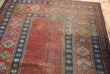 Antique Caucasian carpet's madder red field with visible foundation wear and indigo pawn motif border.