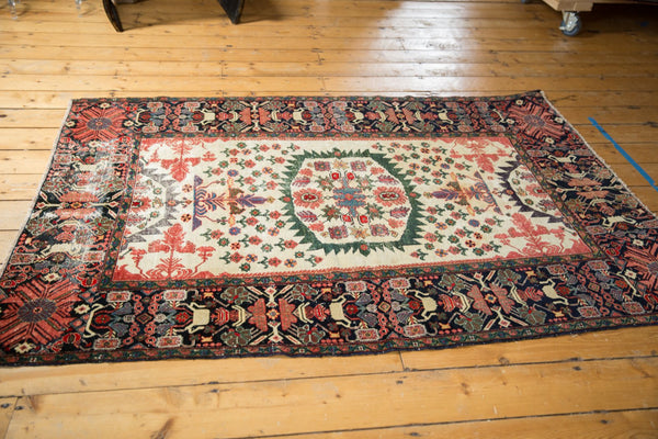 Antique Farahan Sarouk rug shown at an angle, displaying an ivory field, floral medallion, and dark navy border.