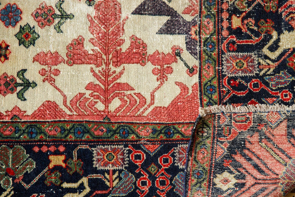 Close-up of an antique Farahan Sarouk rug's corner folded to show the intricate navy border and hand-knotted foundation.