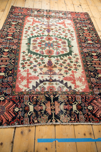 Angled view of an antique Farahan Sarouk rug with a serrated green medallion and wide, dynamic navy border.