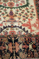 Angled view of the antique Farahan Sarouk rug's serrated medallion outline and detailed navy blue border.