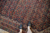 Vintage Shiraz rug showing repeating germinating plant design in navy, brick red, ivory, with visible wear.