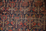 Intricate germinating plant motifs and visible wear on a vintage Shiraz carpet pile.